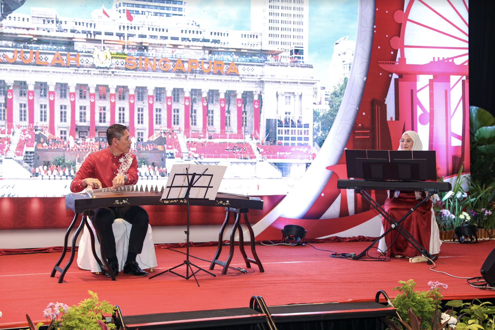 Two musicians perform on a red stage against backdrop images of Singapore.